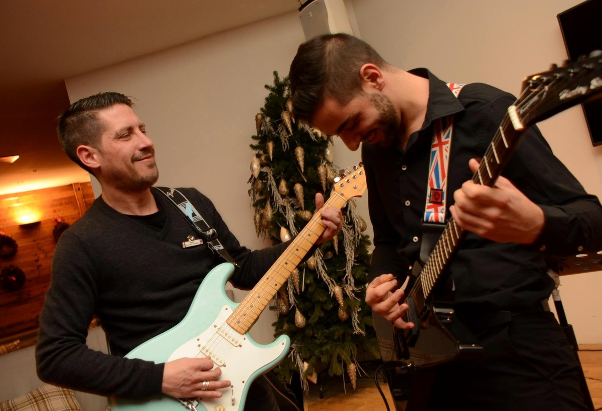 Two guitarists performing together at an indoor event